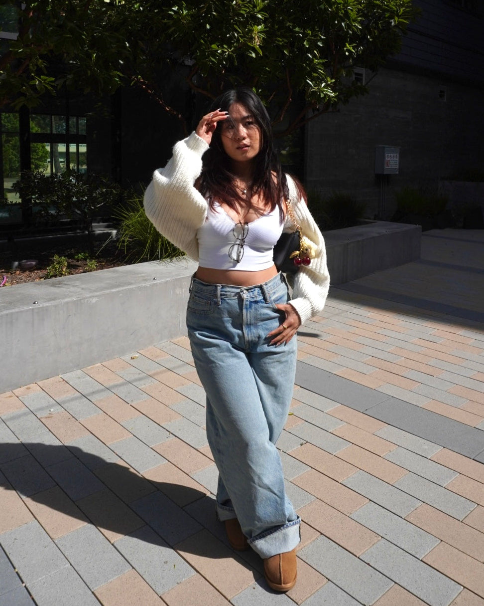 Woman standing outdoors on a paved area with greenery in the background