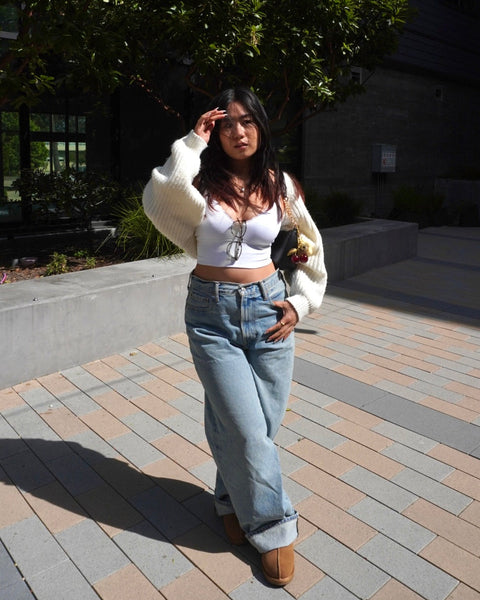 Woman standing outdoors on a paved area with greenery in the background